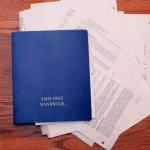 Employee handbook on desk, papers strewn aboutout