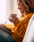 Woman in yellow sweater holding a cup of tea and writing in a notebook while planning her estate